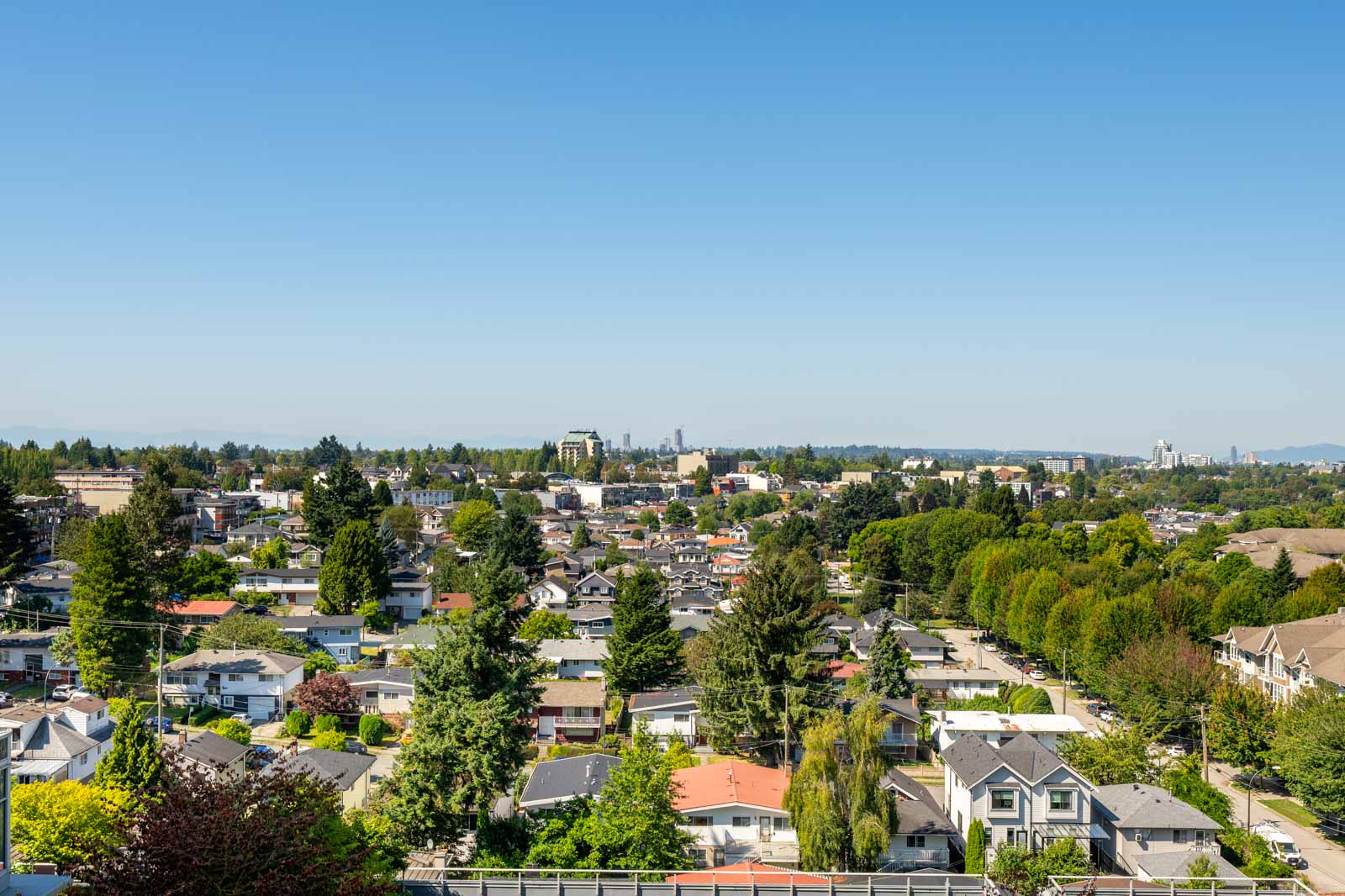 A suburban neighborhood with houses, trees, and clear streets, set under a blue sky with distant city buildings visible on the horizon.