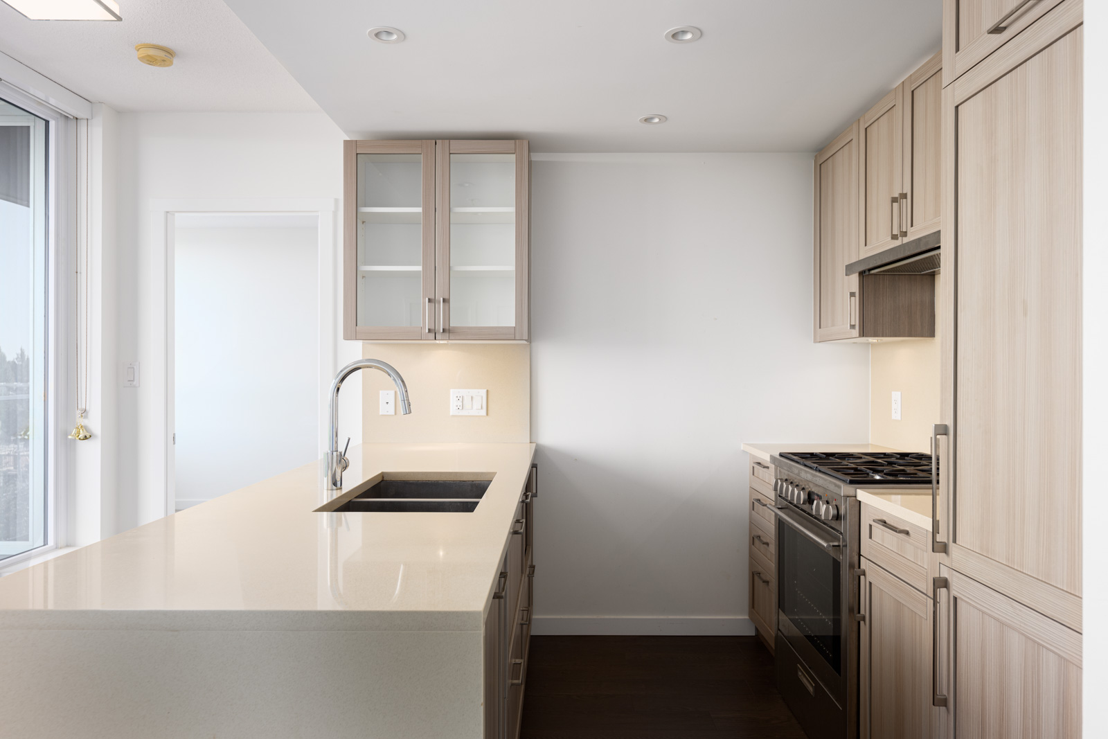 Modern kitchen with light wood cabinets, stainless steel appliances, a gas stove, and a large island featuring a sink and faucet.