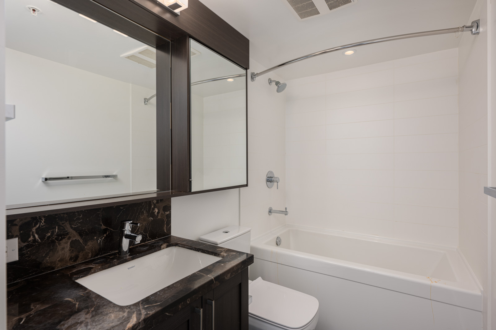 Modern bathroom with a dark marble countertop, undermount sink, large mirror, white bathtub with shower, and towel bar.