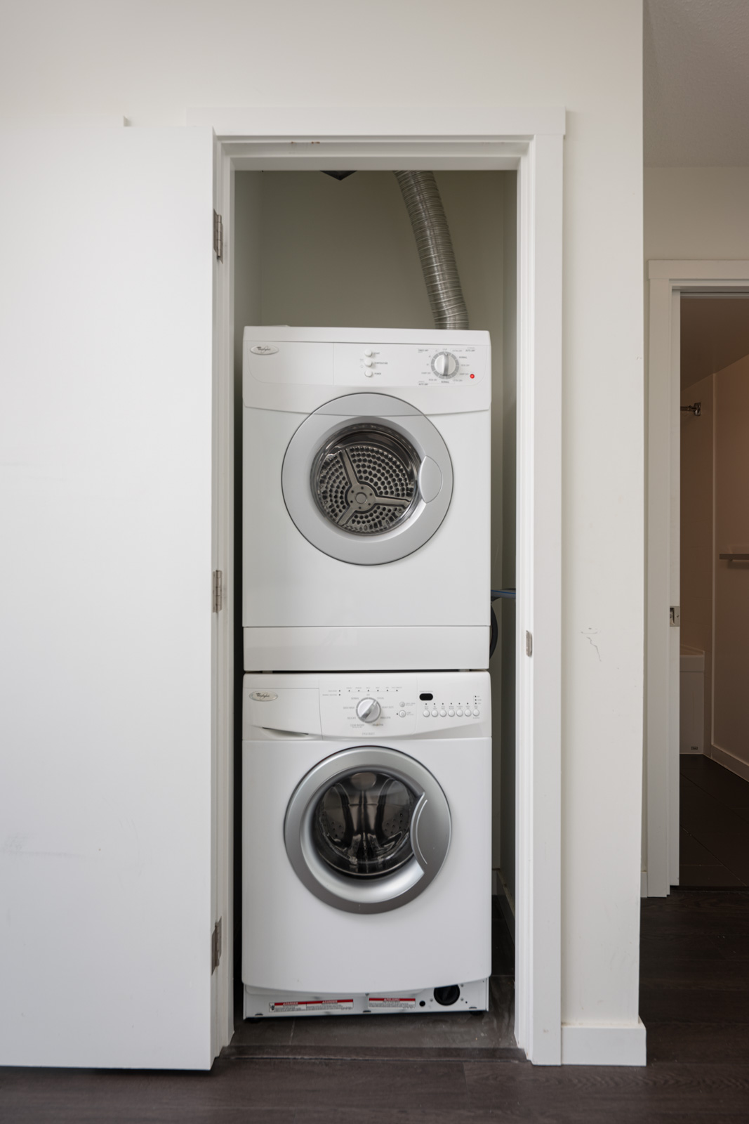 A stacked washer and dryer set is installed in a small closet with a partially open white door.