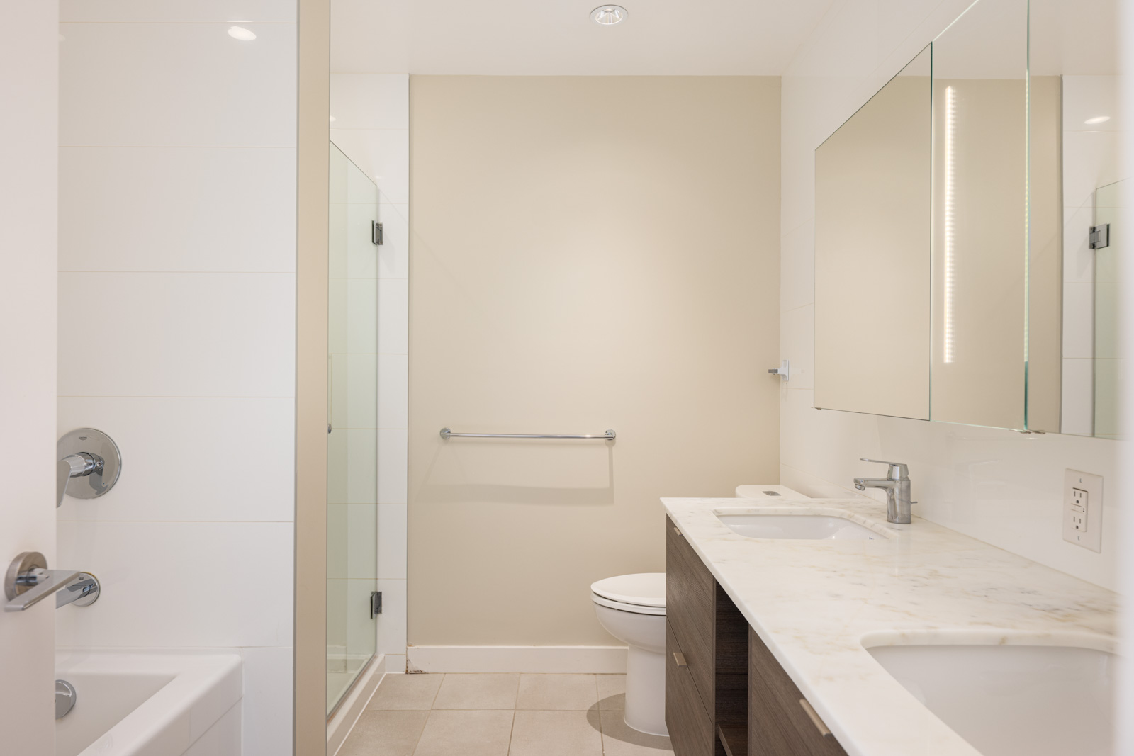 Modern bathroom with a bathtub, glass shower, double sink vanity with marble countertop, wall mirror, toilet, and beige walls.