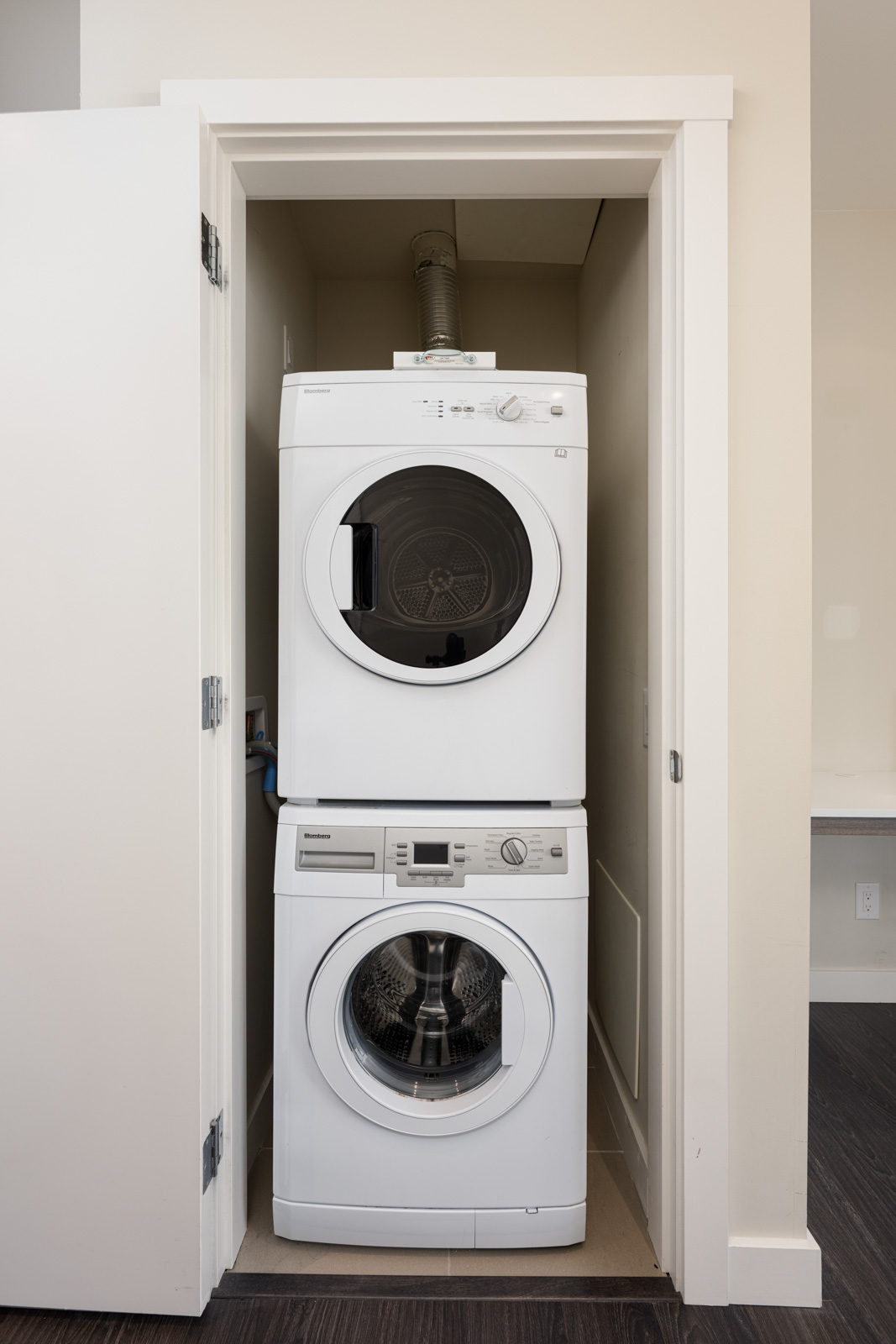 A stacked washer and dryer unit in a small closet with white walls and an open door.