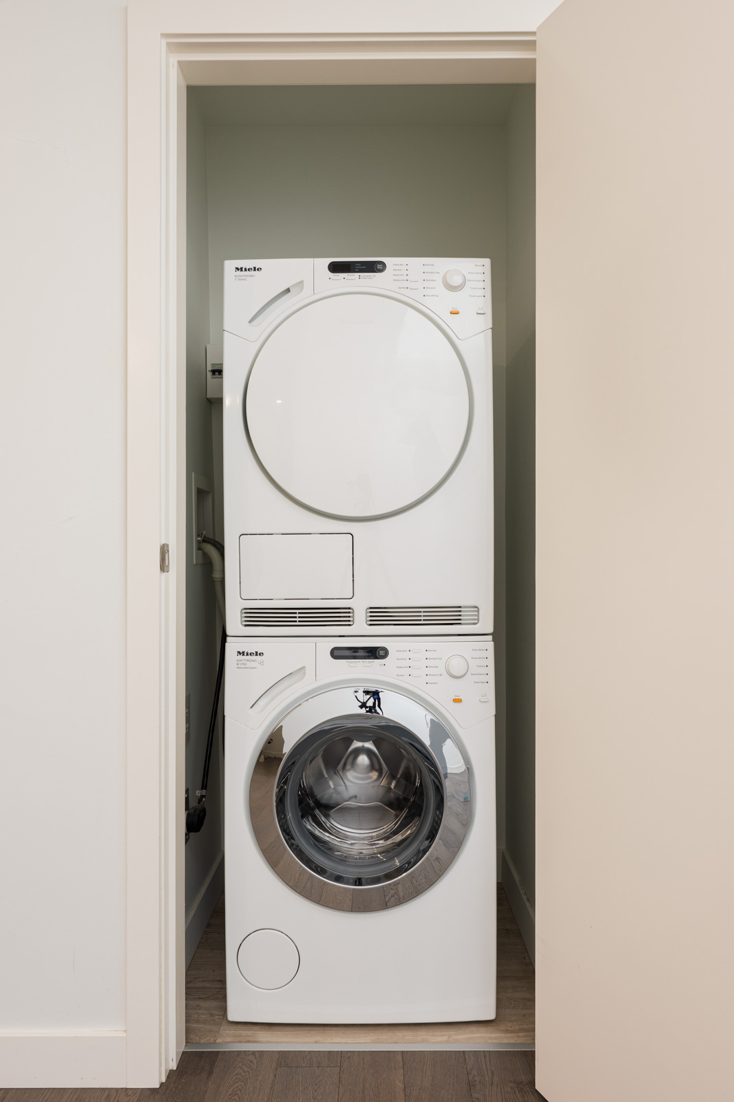 A stacked washer and dryer set is placed inside a small laundry closet with a partially open door.