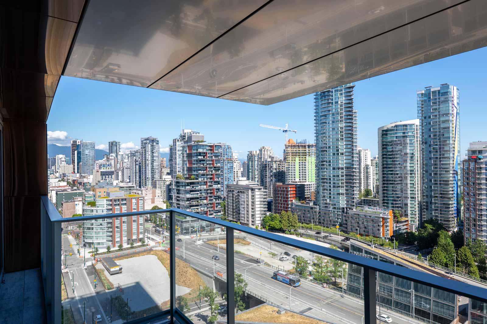 View from a balcony overlooking a cityscape filled with modern high-rise buildings and construction cranes under a clear blue sky.