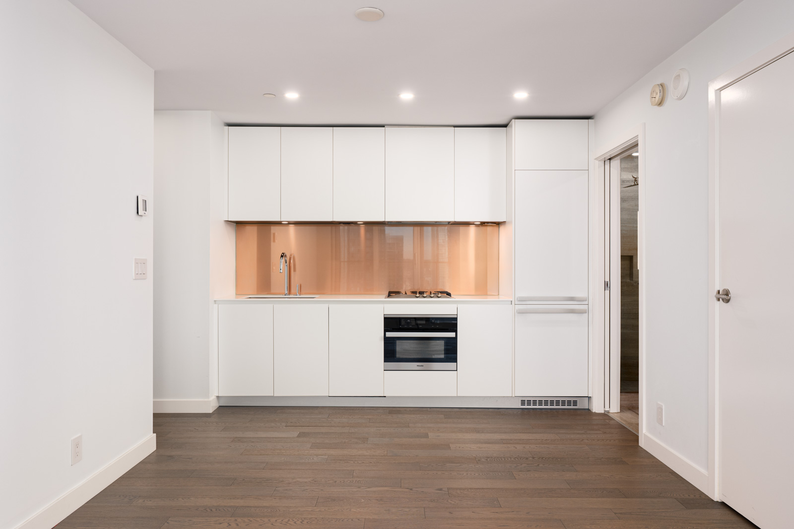 Modern kitchen with white cabinets, built-in oven, stovetop, and sink. Light wood flooring and neutral wall colors create a minimalist, clean look.