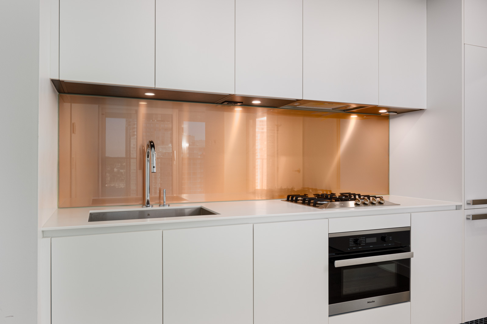 Modern kitchen with white cabinets, a stainless steel sink, a built-in oven, a gas cooktop, and a glossy light brown backsplash.