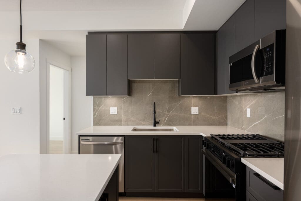 Modern kitchen with dark cabinets, stainless steel appliances, a marble backsplash, a single pendant light, and a white countertop island.