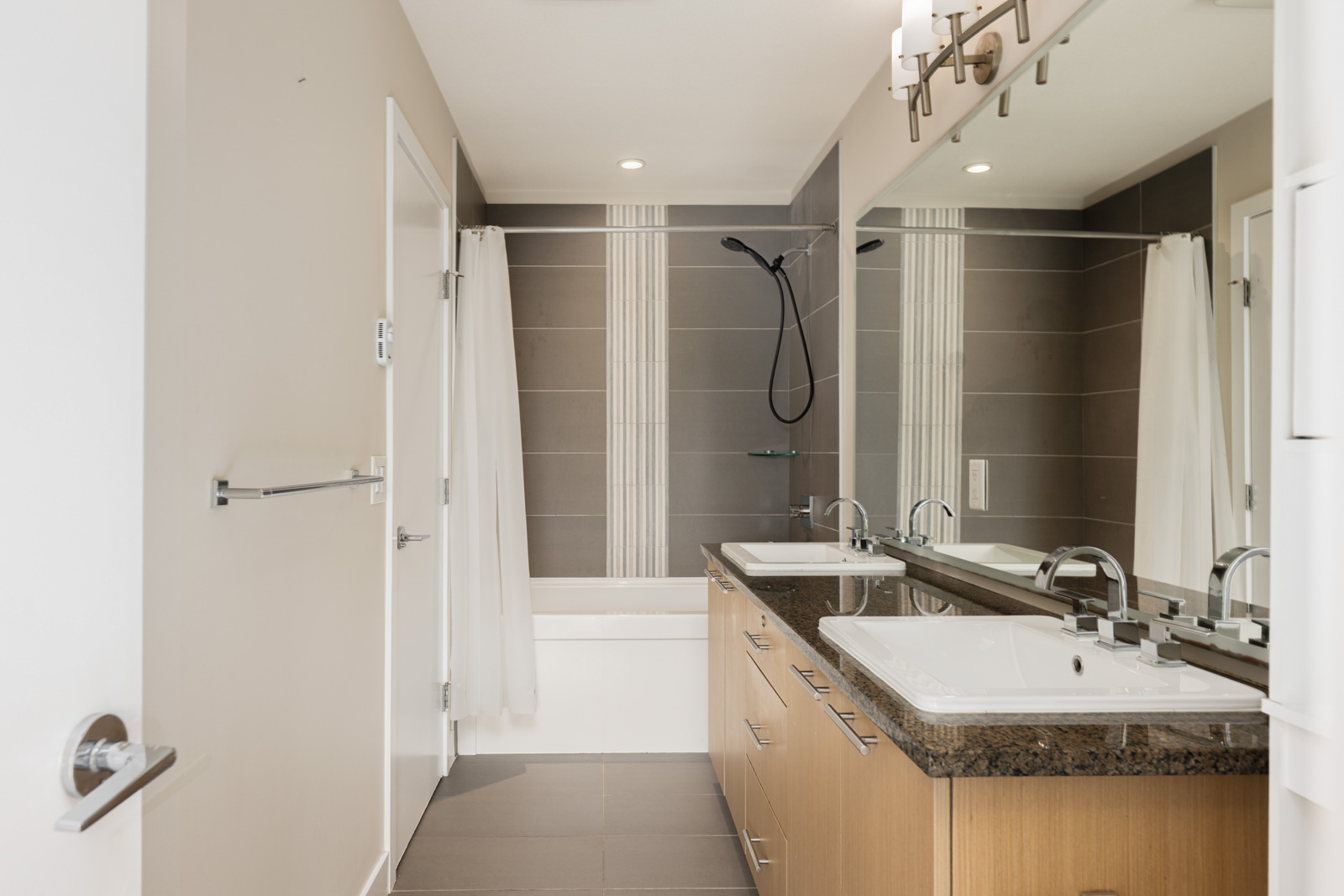 Modern bathroom with double sinks, wood vanity, large mirror, and a bathtub with a shower and white curtain. Neutral color palette with gray and beige tones.