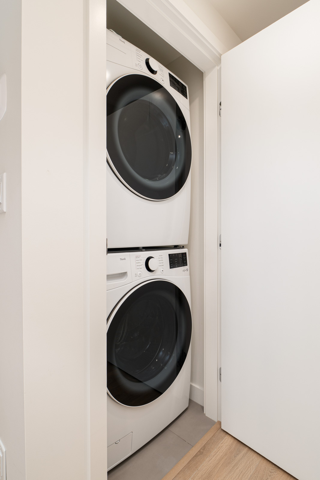 A stacked washer and dryer unit is installed in a small laundry closet with a white door partially open.