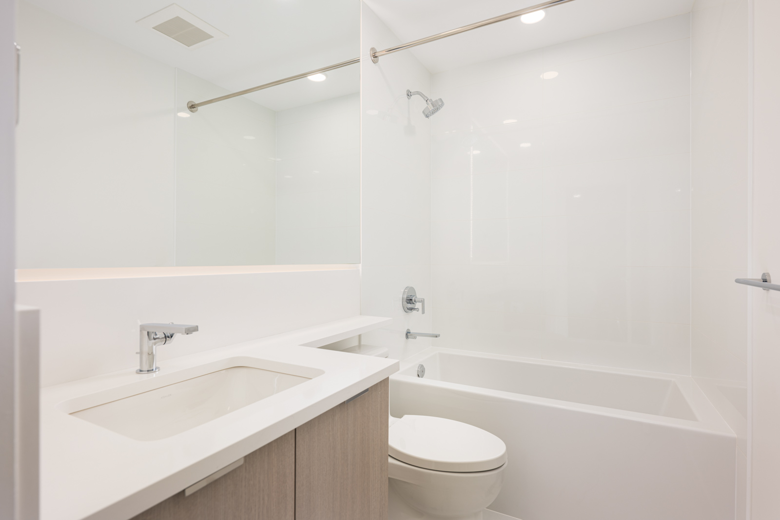 Modern bathroom with a white countertop sink, toilet, bathtub-shower combination, and minimalistic fixtures.