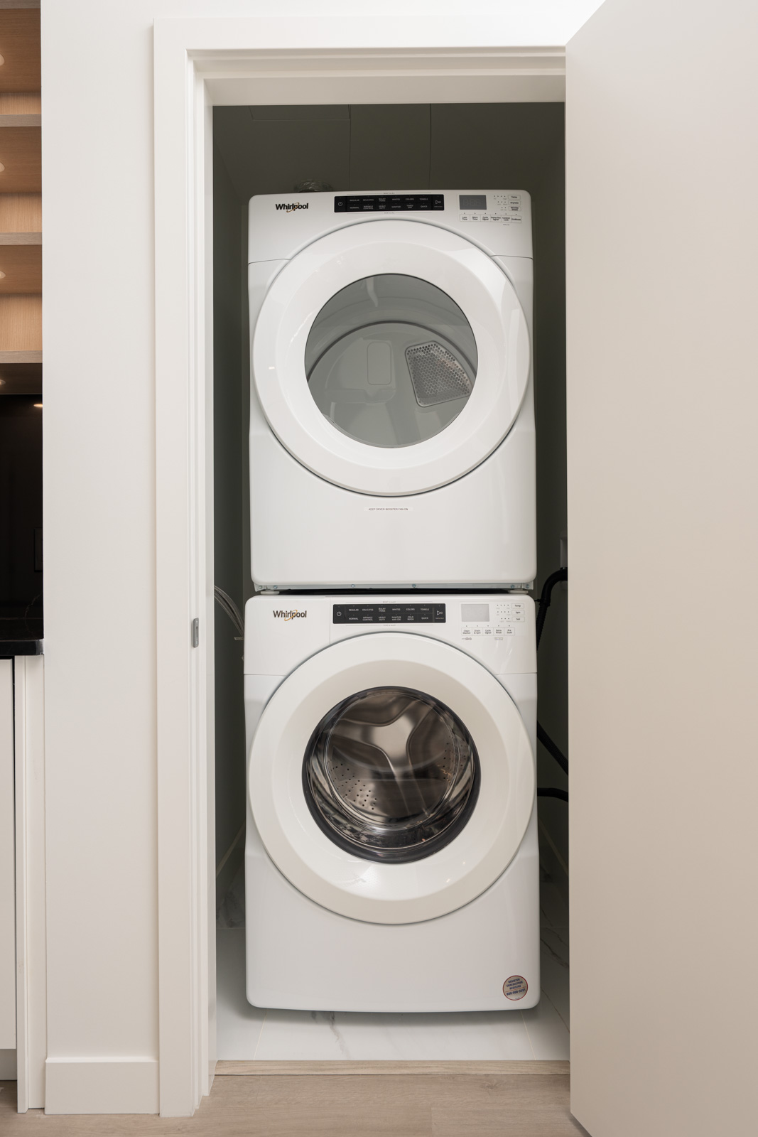 A stacked white Whirlpool washer and dryer set is installed inside a small closet with open double doors.