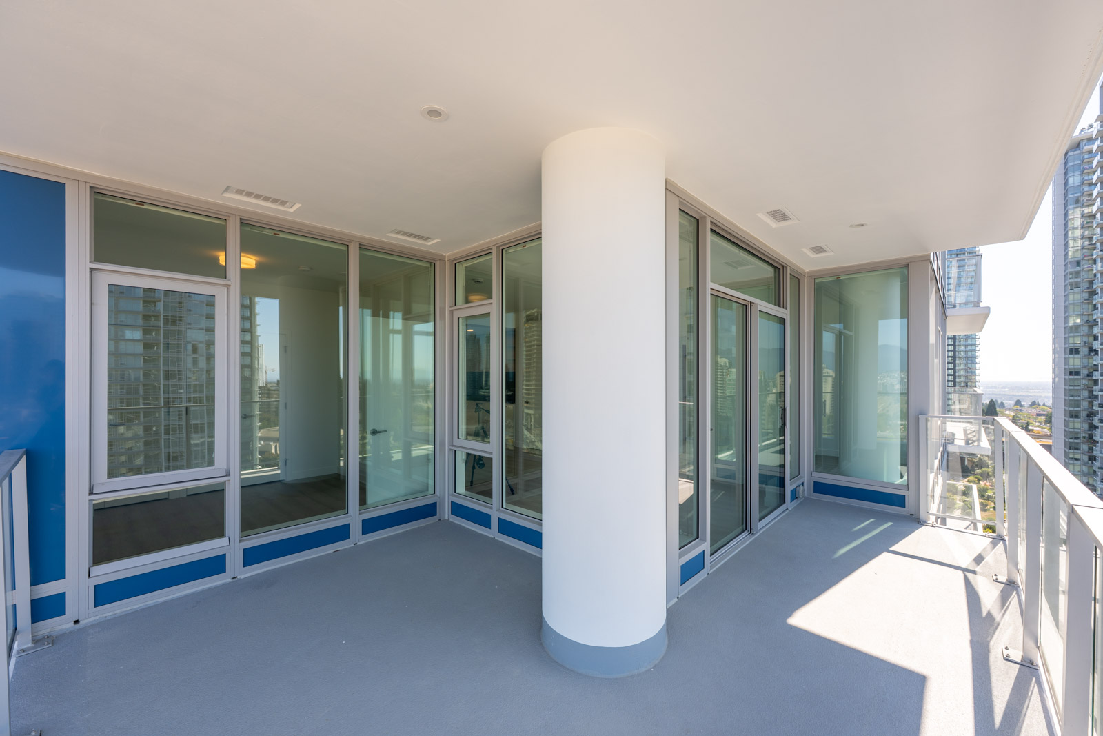 Spacious balcony of a modern high-rise apartment with glass railings, floor-to-ceiling windows, and a large central column.
