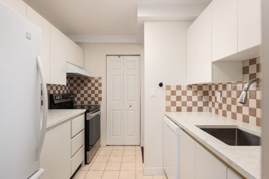 A modern kitchen with white cabinets, checkered beige backsplash, white appliances, a sink, and a double-door pantry.