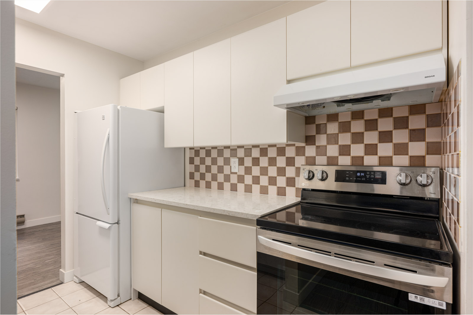 A modern kitchen with white cabinets, a white refrigerator, an electric stove with an overhead range hood, and a beige checkered tile backsplash.