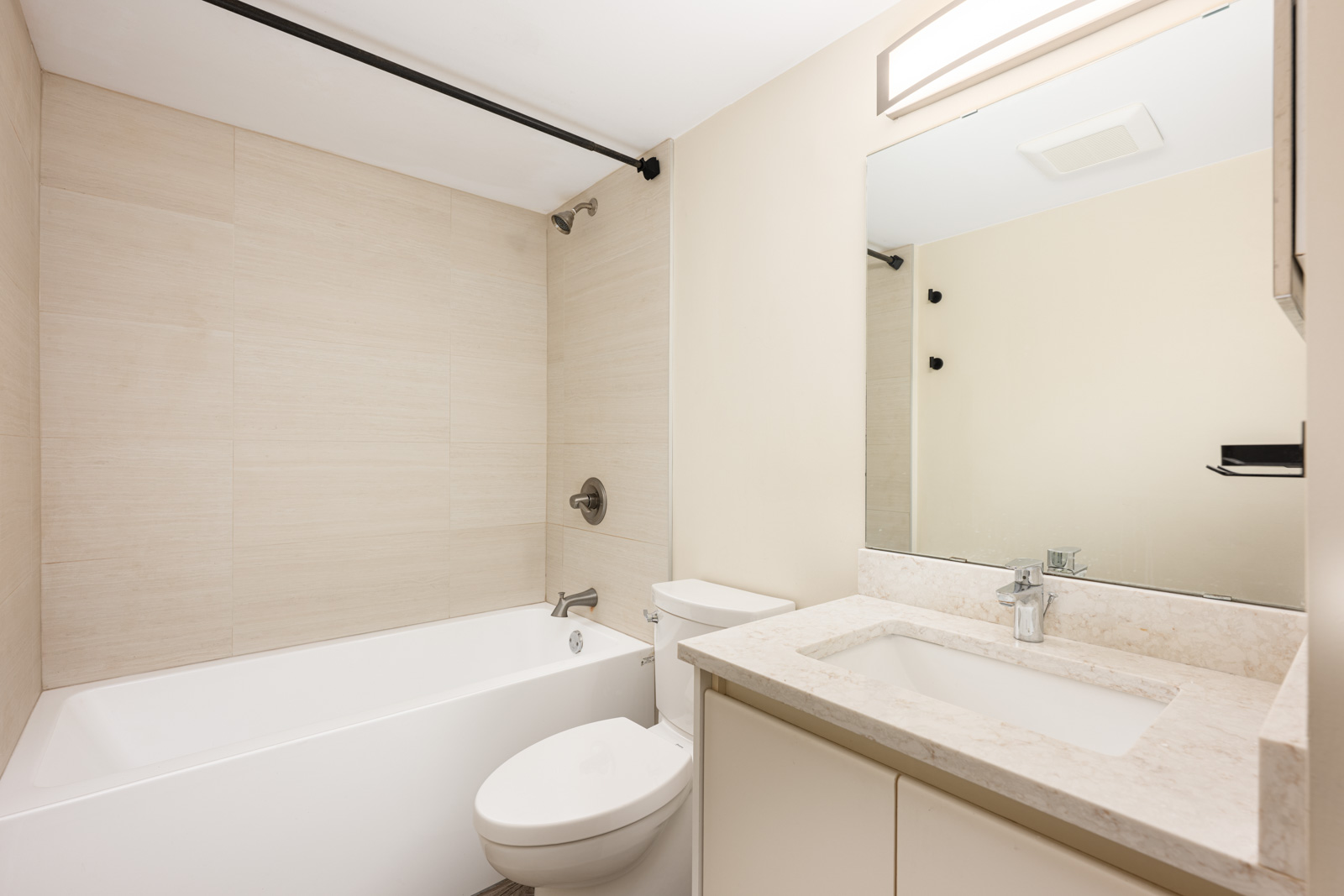 Modern bathroom with a bathtub, toilet, and sink vanity with a large mirror. Light walls and tiles create a clean, minimalist look.
