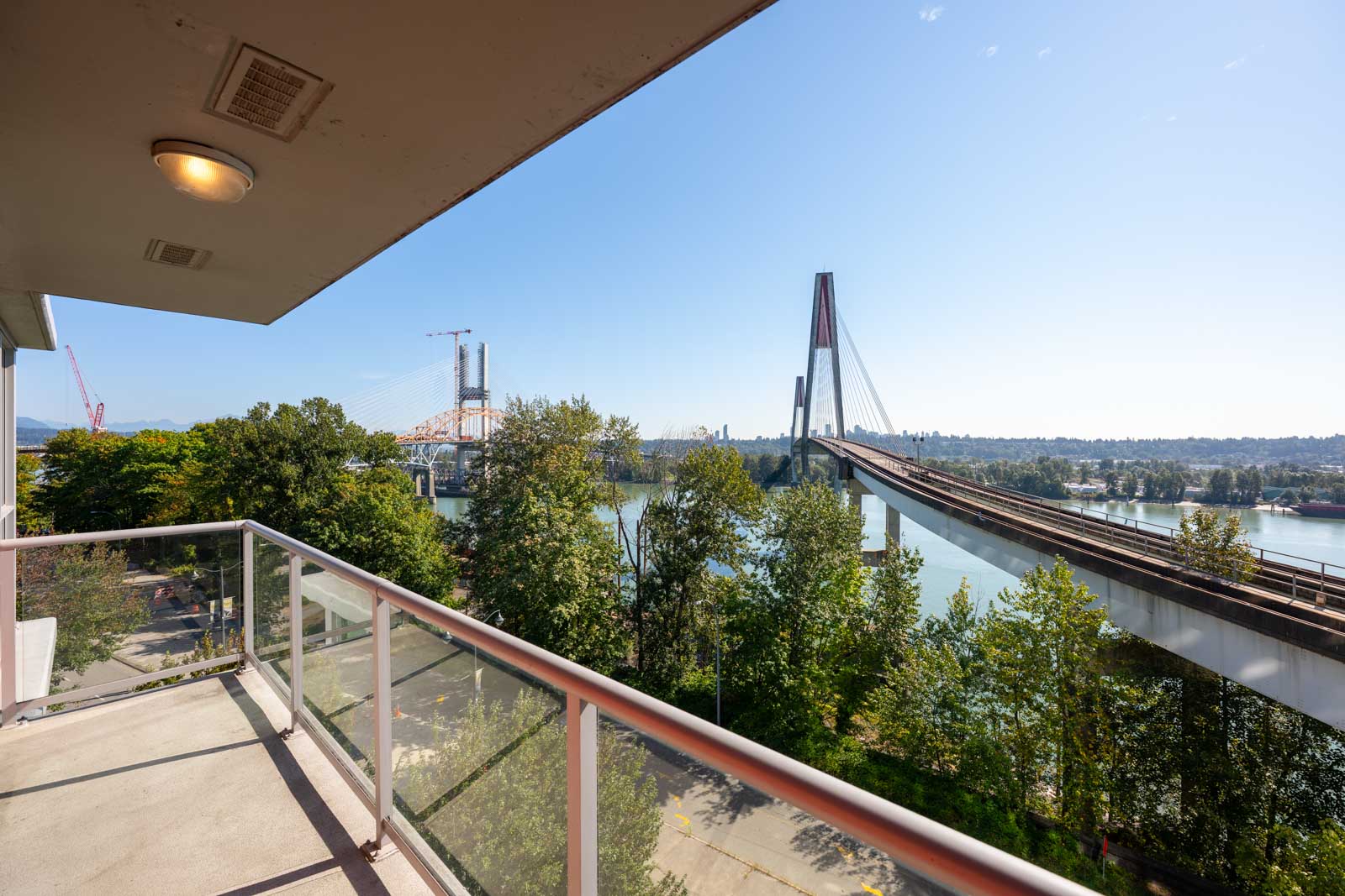 View from a balcony overlooking a river, with a cable-stayed bridge and trees under a clear blue sky.