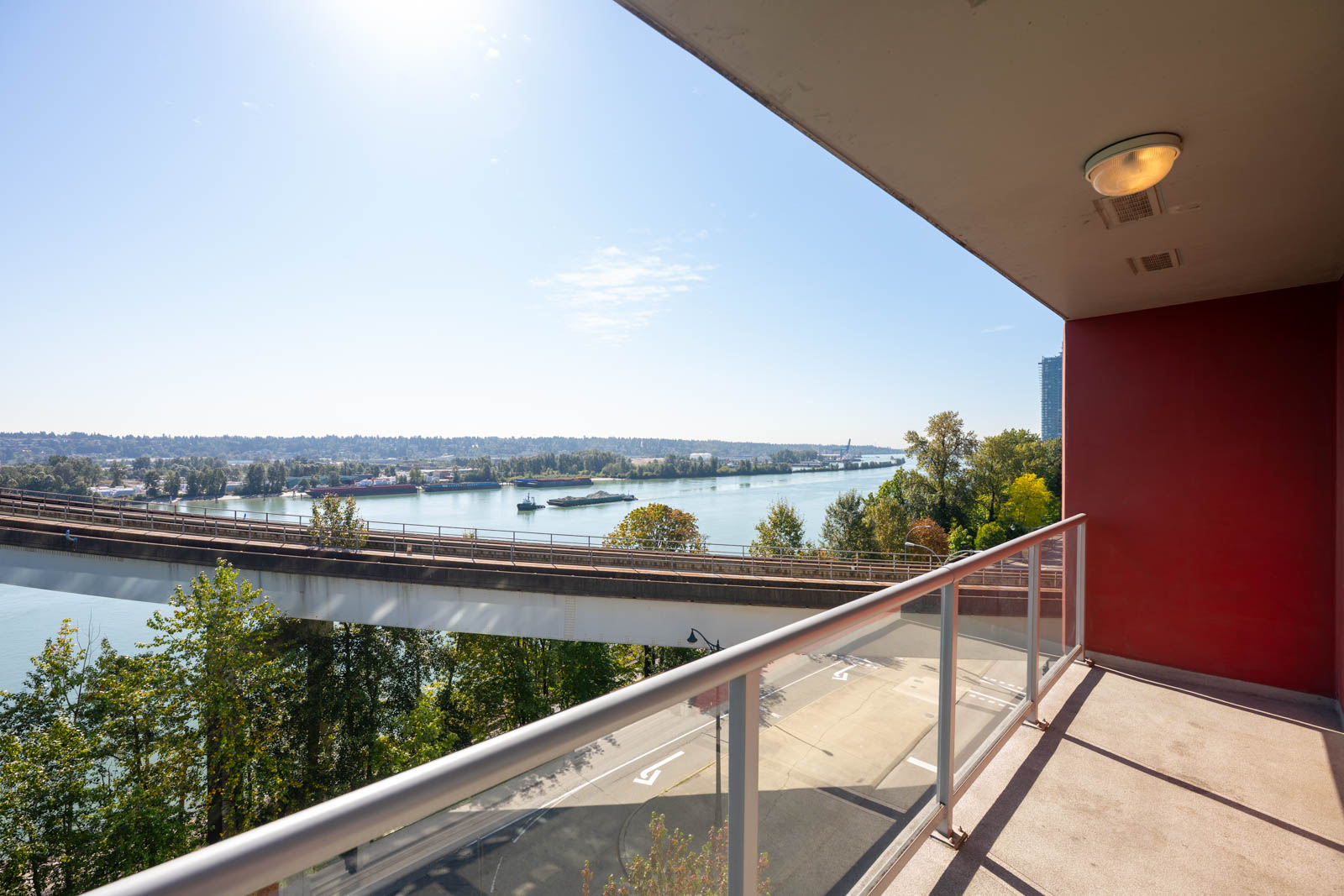 View from a balcony overlooking a river, elevated road, trees, and a clear sky on a sunny day.