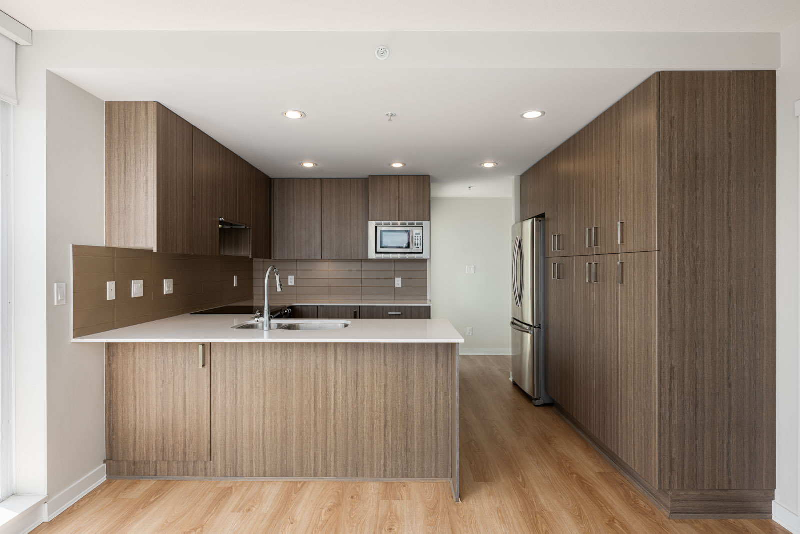 Modern kitchen with wood cabinets, stainless steel appliances, built-in microwave, double sink, and a white countertop island on a light wood floor.