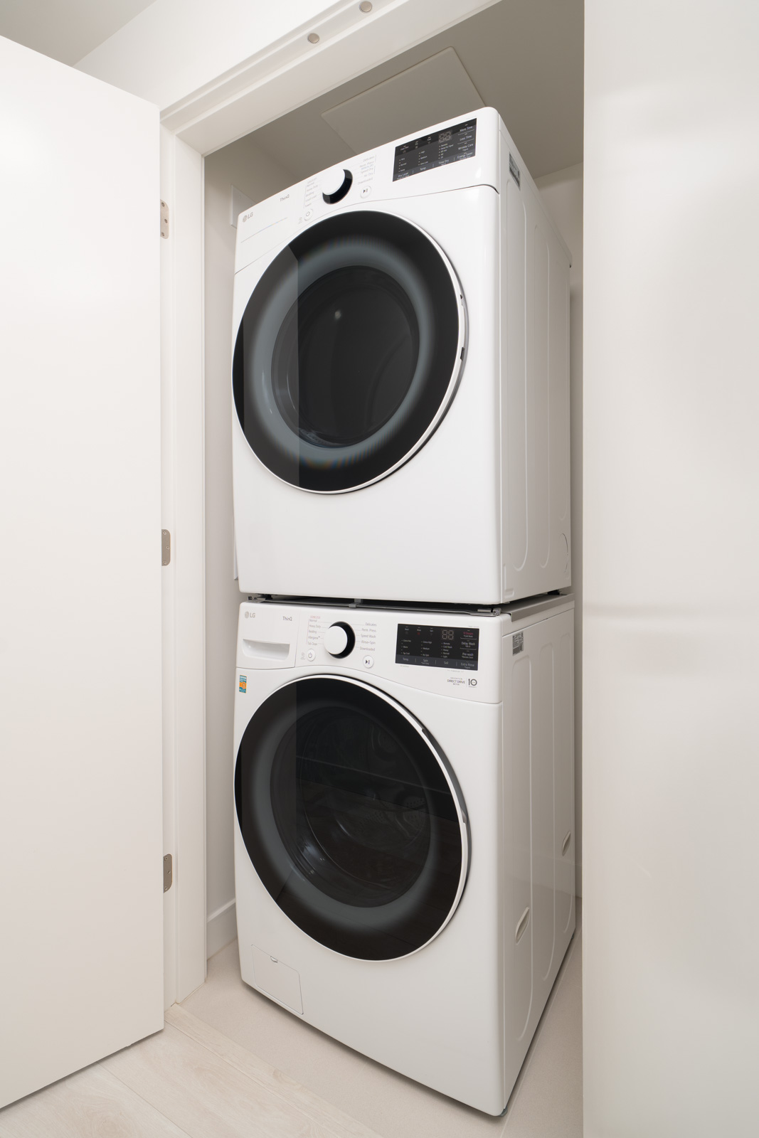 A stacked washer and dryer set is installed in a small, white laundry closet with the door open.