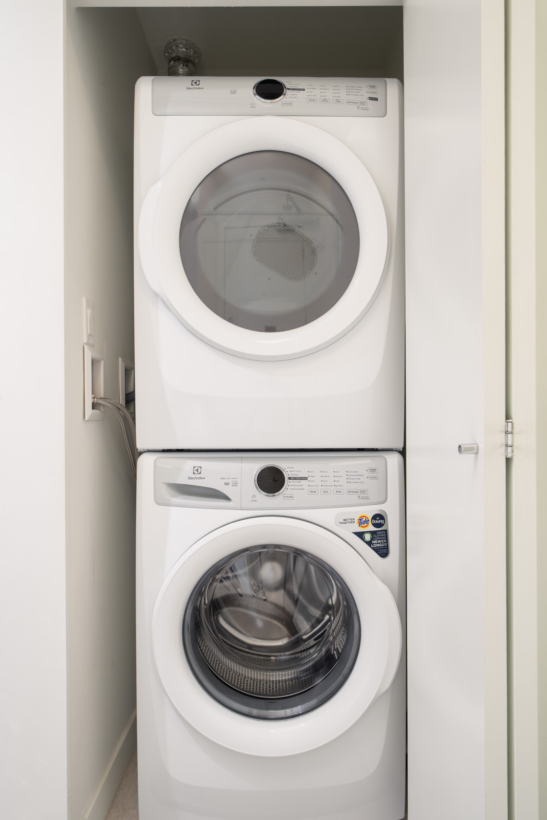 A stacked white washer and dryer set installed in a small closet space with white walls.