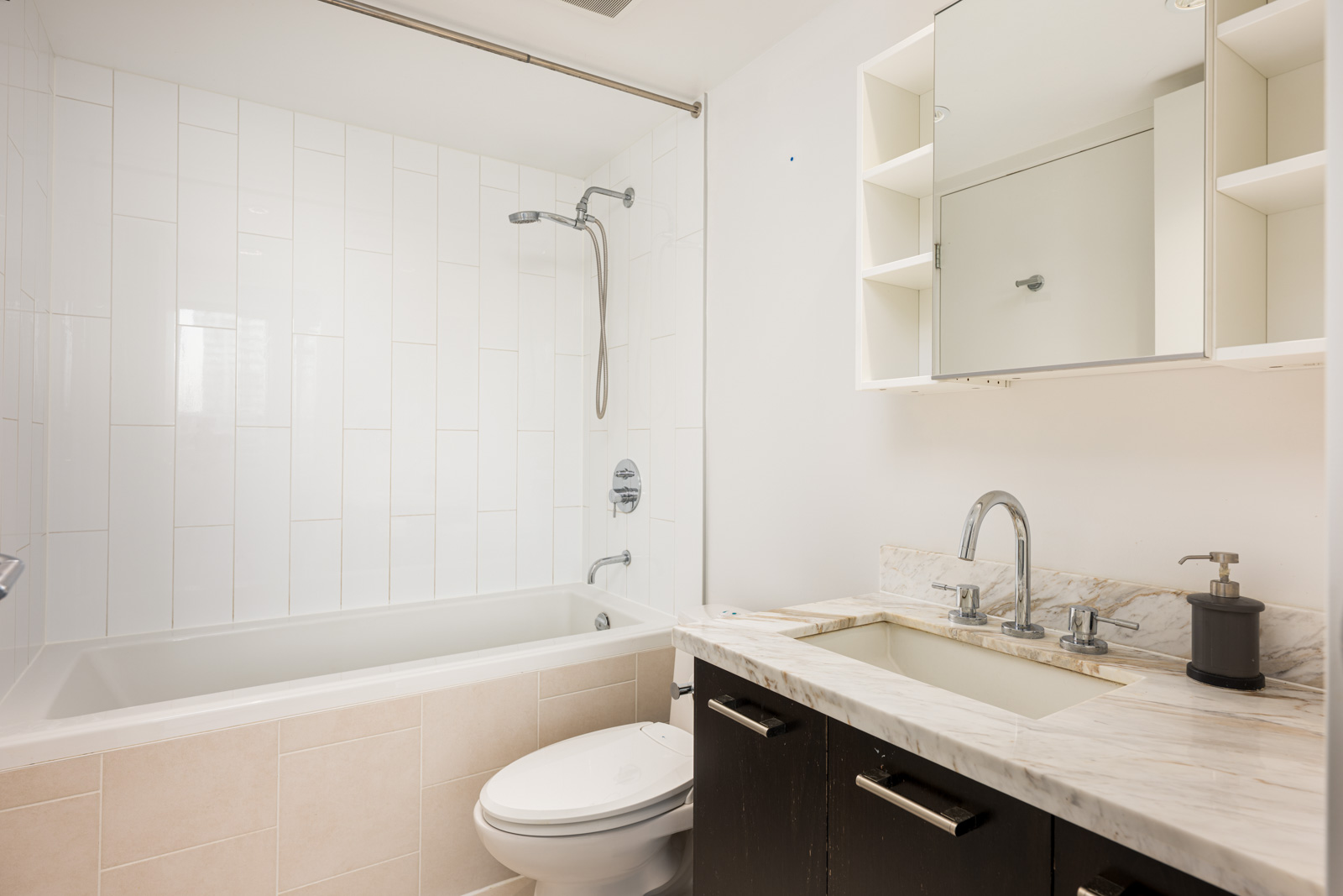 Modern bathroom with a bathtub-shower combination, toilet, and a vanity with a marble countertop, under a mirrored cabinet.
