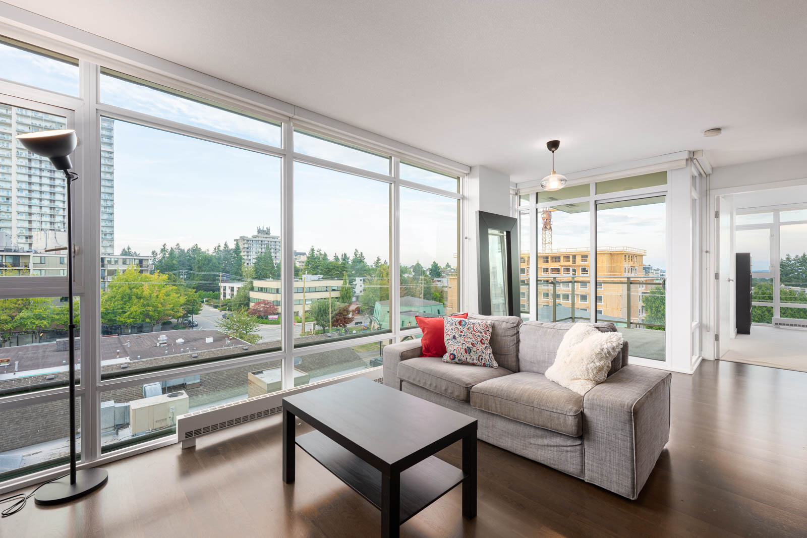 A modern living room with large floor-to-ceiling windows, a gray sofa, a black coffee table, and cityscape views in the background.