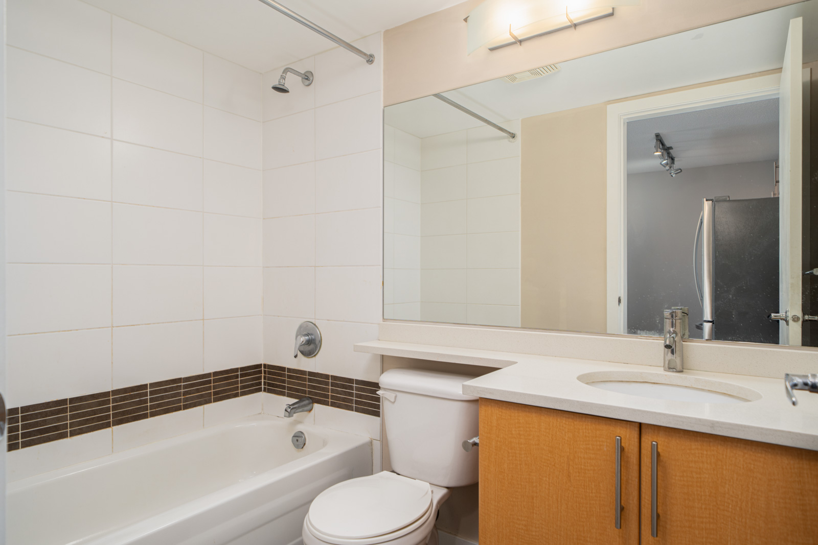 Modern bathroom with a bathtub, shower, toilet, large mirror, and wooden vanity with sink under bright overhead lighting.