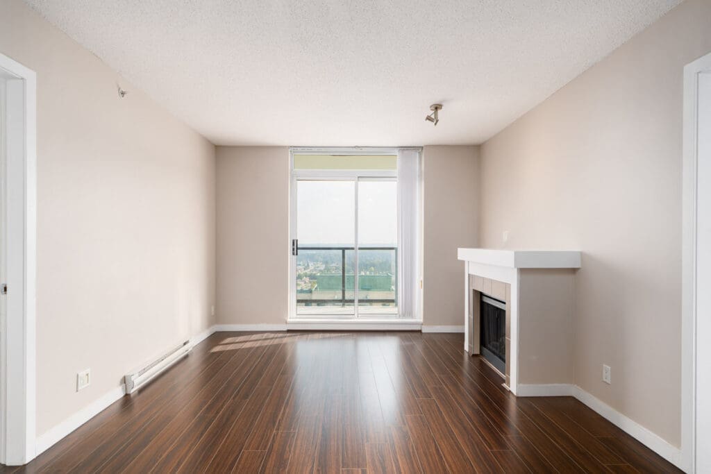 Unfurnished room with wood floors, beige walls, a modern fireplace, and a sliding glass door leading to a balcony with a view.