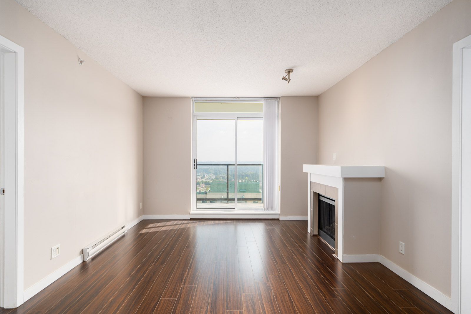 Unfurnished room with wood floors, beige walls, a modern fireplace, and a sliding glass door leading to a balcony with a view.