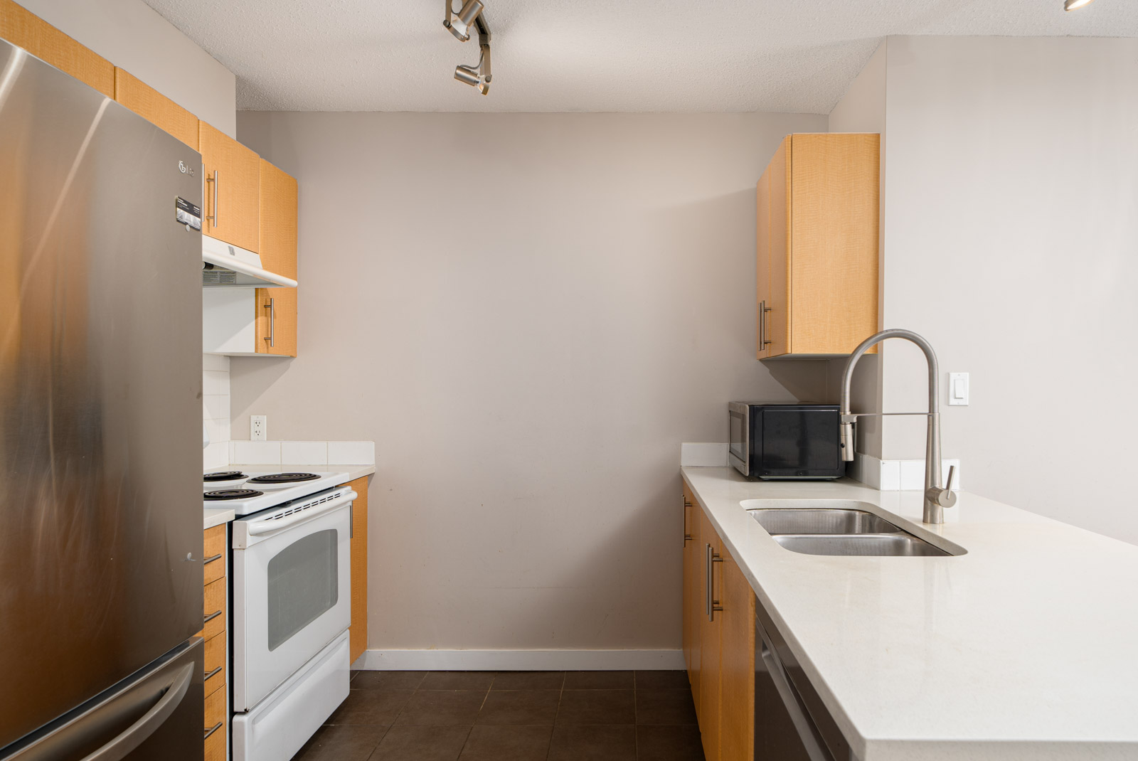 Modern kitchen with stainless steel refrigerator, white stove, microwave, sink, and light wood cabinets against neutral walls.
