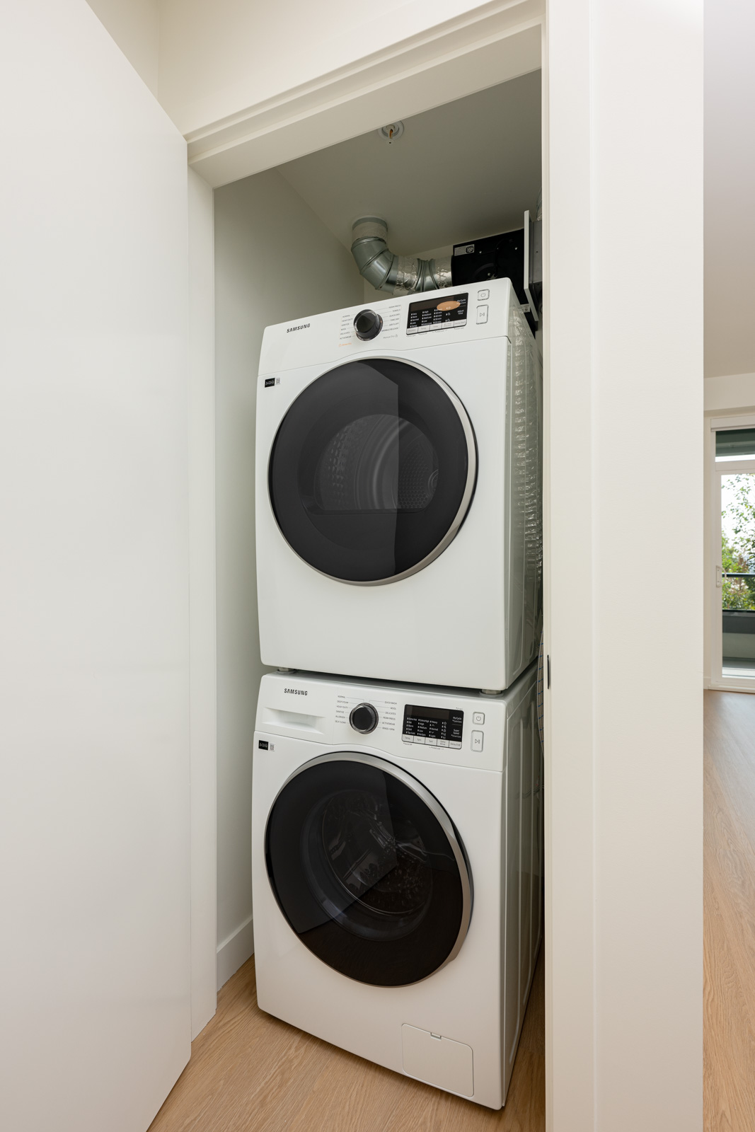 A stacked washer and dryer set is installed in a compact laundry closet with white walls and a sliding door.