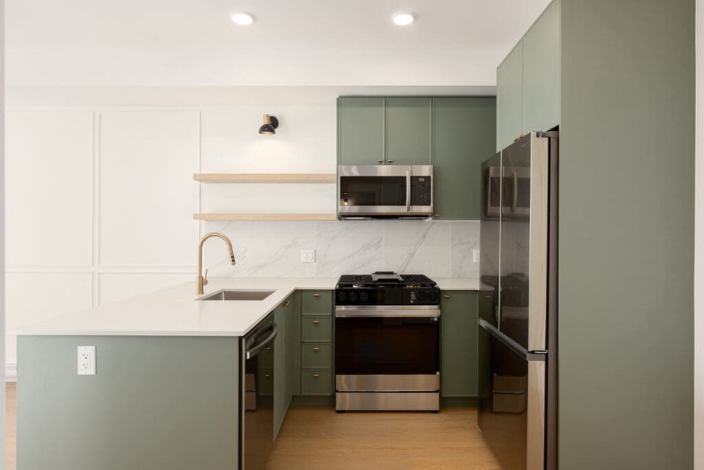 Modern kitchen with sage green cabinets, white countertops, stainless steel appliances, a built-in oven, open shelves, and a marble backsplash.