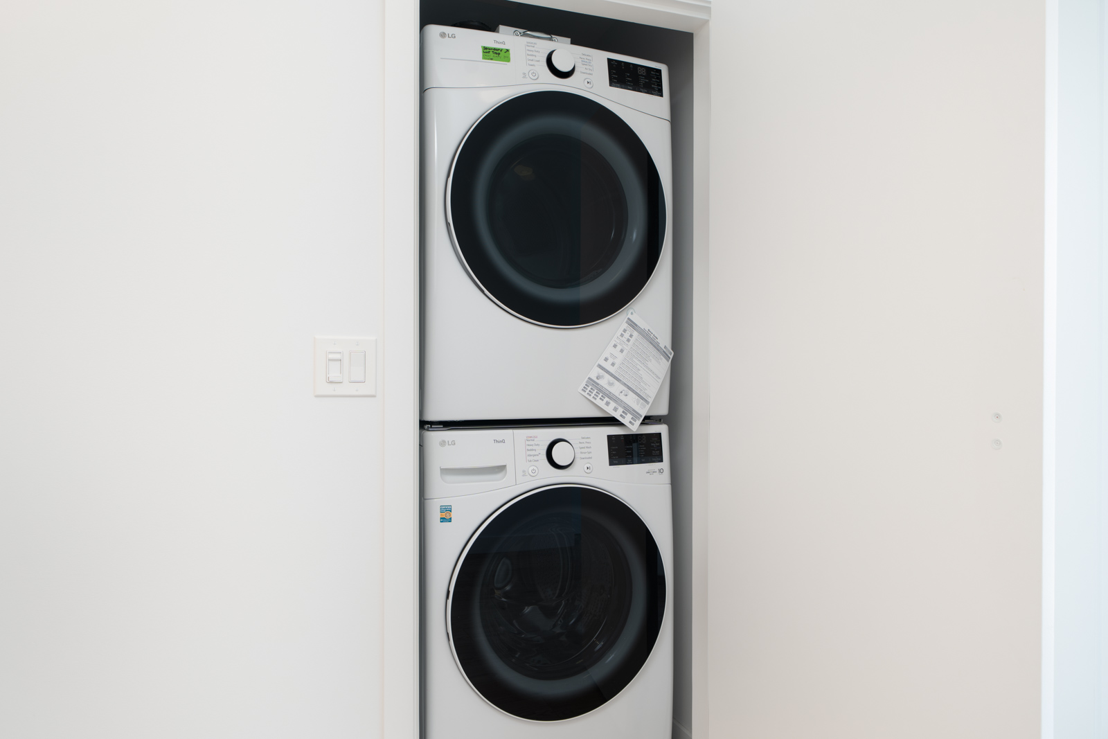 A stacked washer and dryer set is installed in a small laundry closet with white walls.