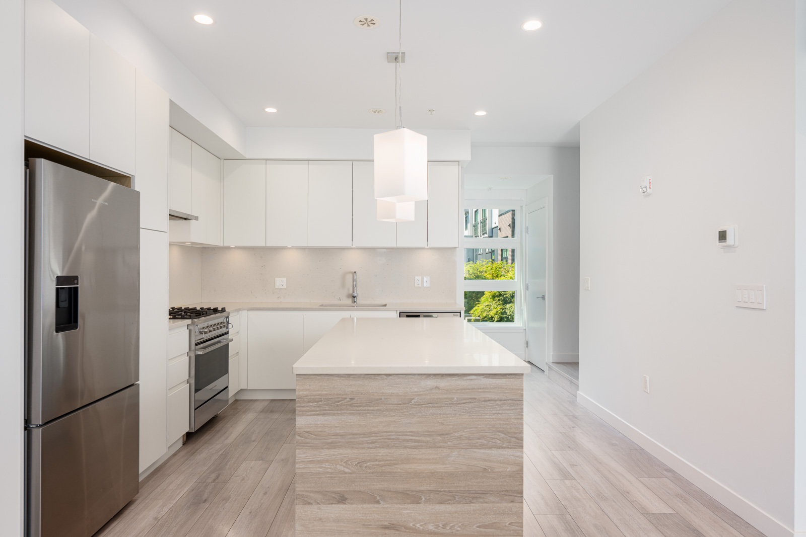 Modern kitchen with white cabinets, stainless steel appliances, a central island with light wood finish, and light wood flooring. Bright space with recessed lighting and pendant lights.