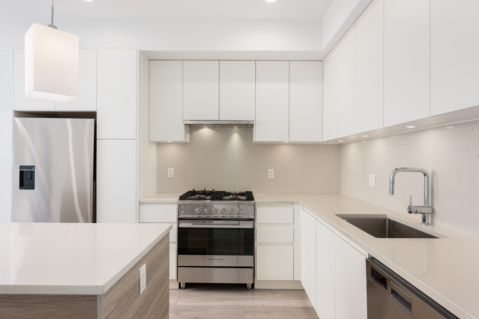 Modern kitchen with white cabinets, stainless steel appliances, gas stove, under-cabinet lighting, and a large sink under bright overhead lighting.
