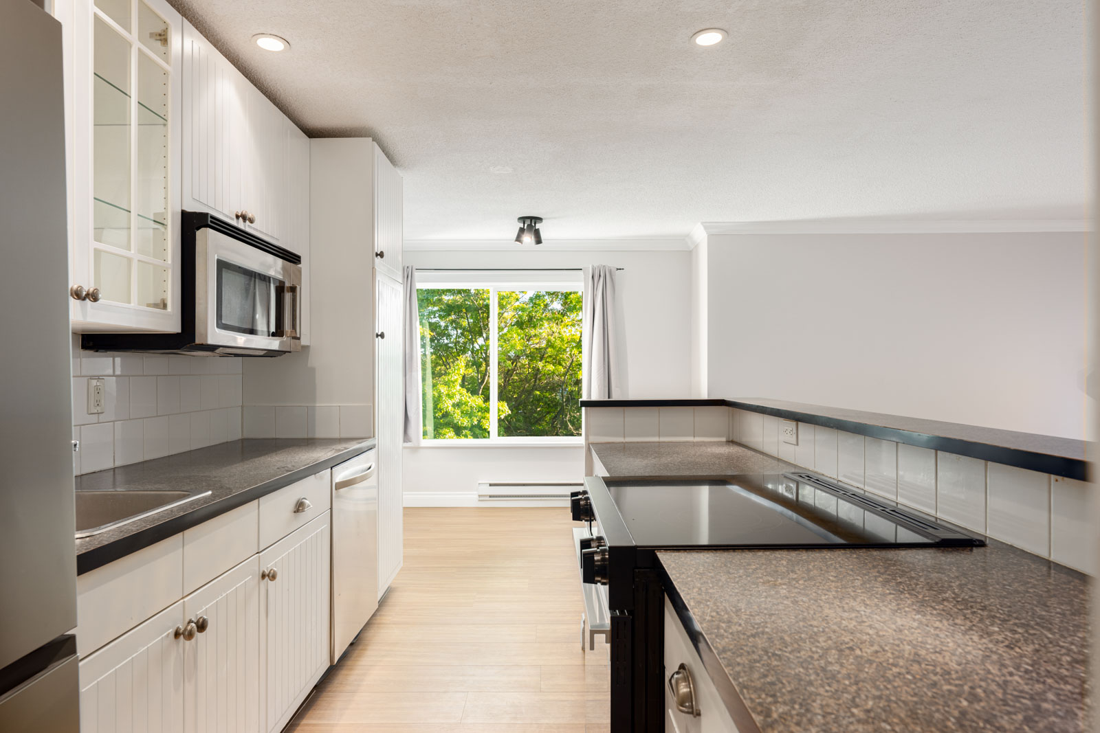 Modern kitchen with white cabinets, black countertops, built-in appliances, and a large window letting in natural light.