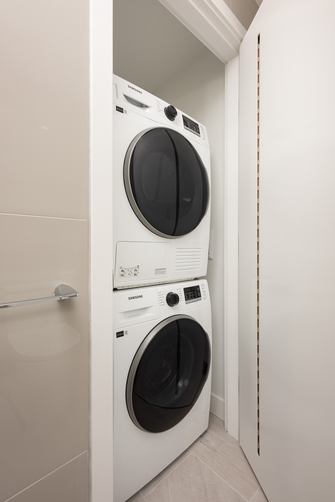 A stacked Samsung washer and dryer set is installed in a narrow closet with white walls and a partially open door.