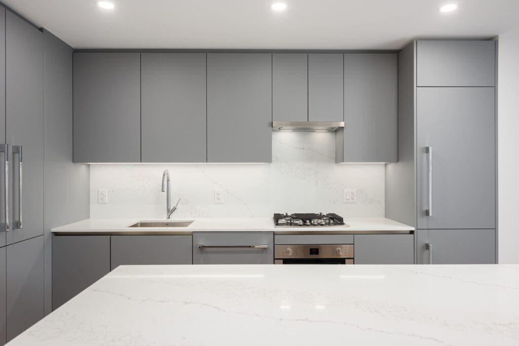 Modern kitchen with matte gray cabinets, built-in appliances, white countertops, gas stove, and under-cabinet lighting. The overall design is minimalist and uncluttered.