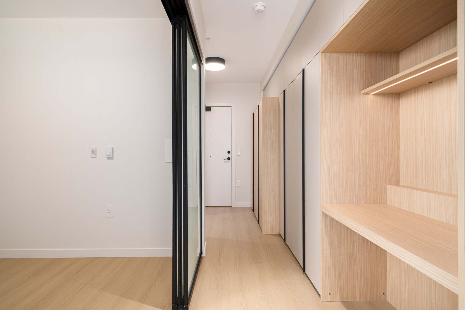 A hallway with white walls and wood floor.