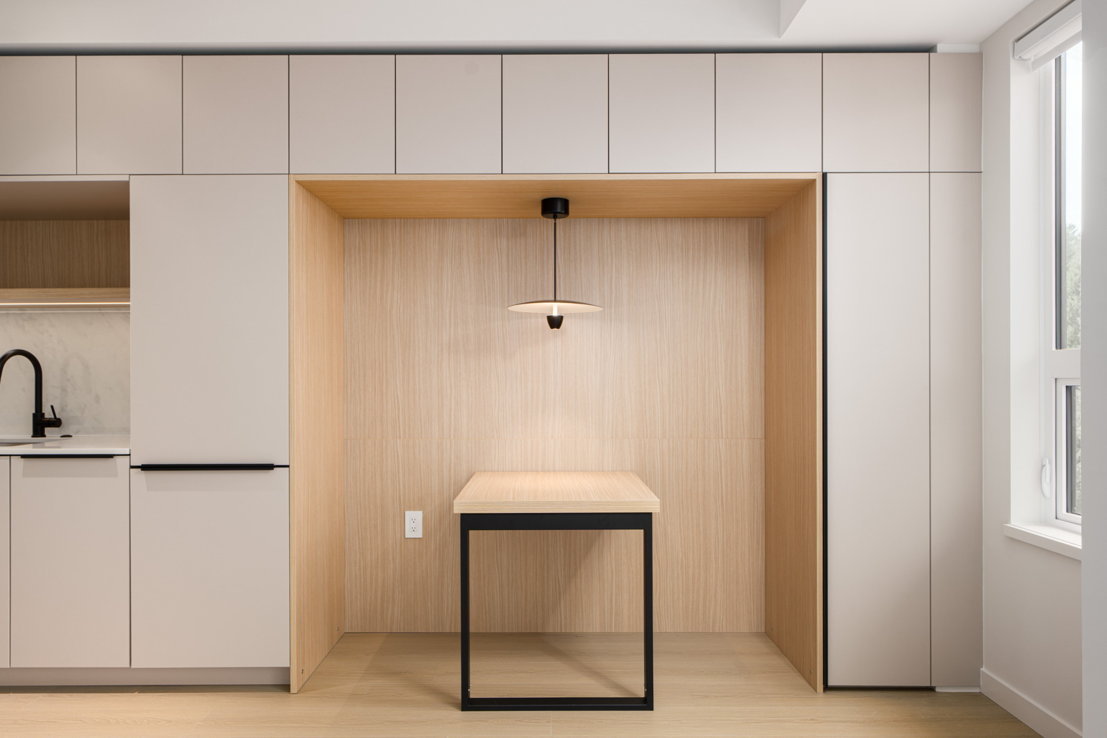 Minimalist kitchen nook with light wood paneling, a small rectangular table, a modern pendant light, and built-in cabinetry surrounding the area.