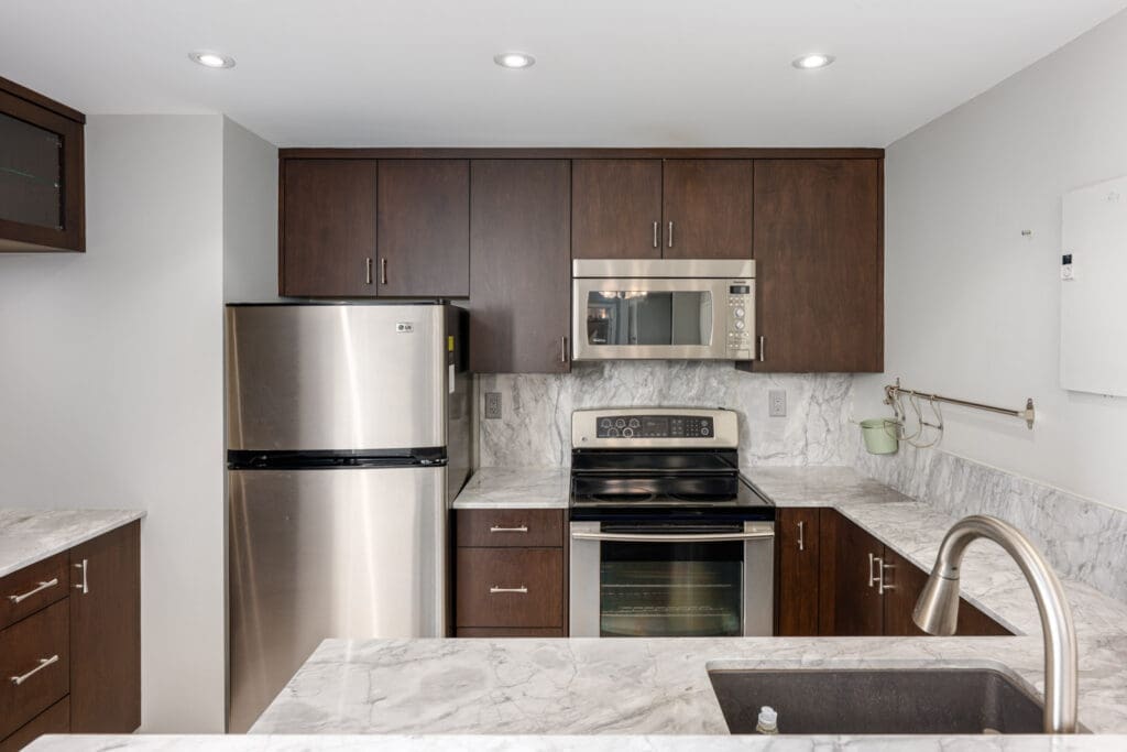 Modern kitchen with dark wood cabinets, stainless steel appliances, marble countertops, an electric stove, and a double sink.