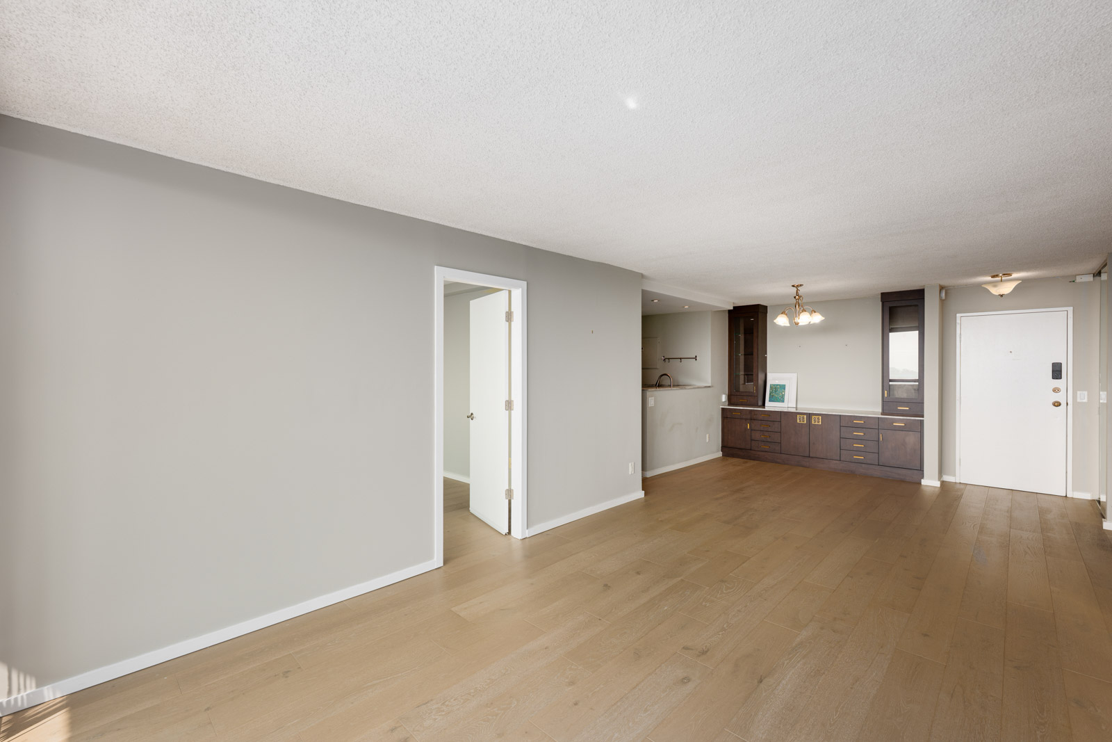 Unfurnished living room with light wood flooring, beige walls, built-in cabinetry, and two white doors—one open to another room and one leading to the entryway.