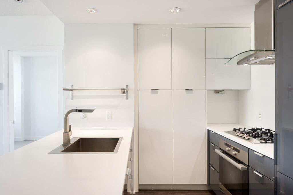 Modern kitchen with white cabinets, built-in oven, gas stovetop, stainless steel sink, and minimalist fixtures.