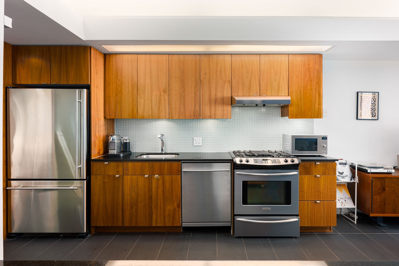 Modern kitchen with stainless steel appliances, wooden cabinets, a refrigerator, dishwasher, oven, microwave, and a small backsplash.