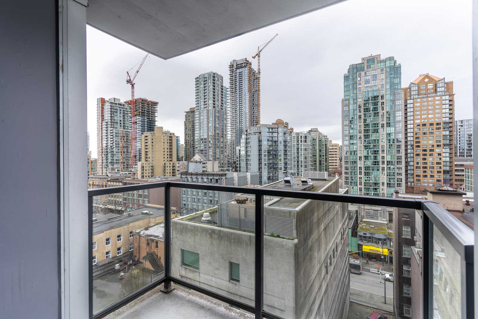 View from a balcony with glass railing overlooking a cityscape of high-rise buildings and construction cranes under a cloudy sky.
