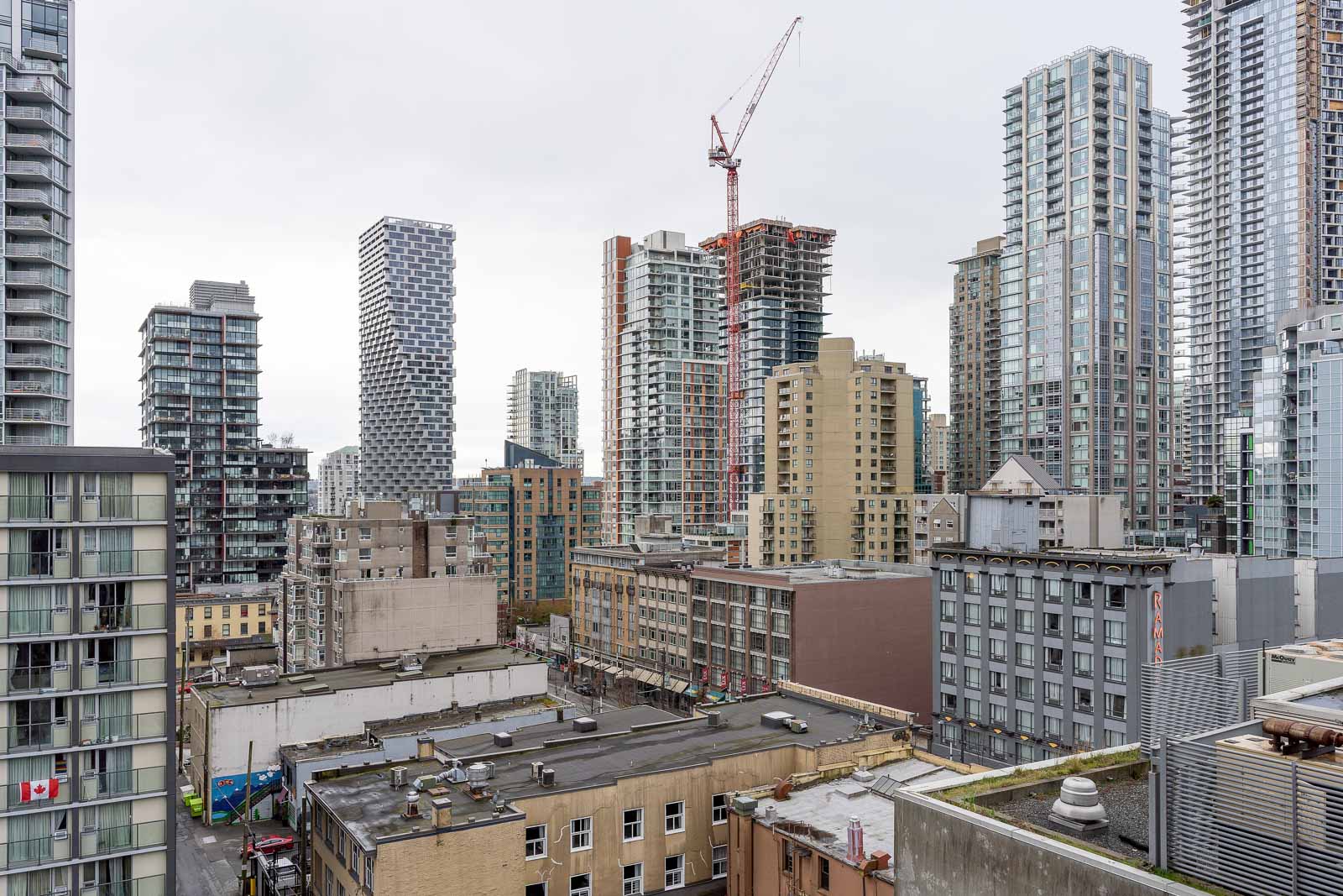 Cityscape view with high-rise buildings and a construction crane among completed towers under an overcast sky.