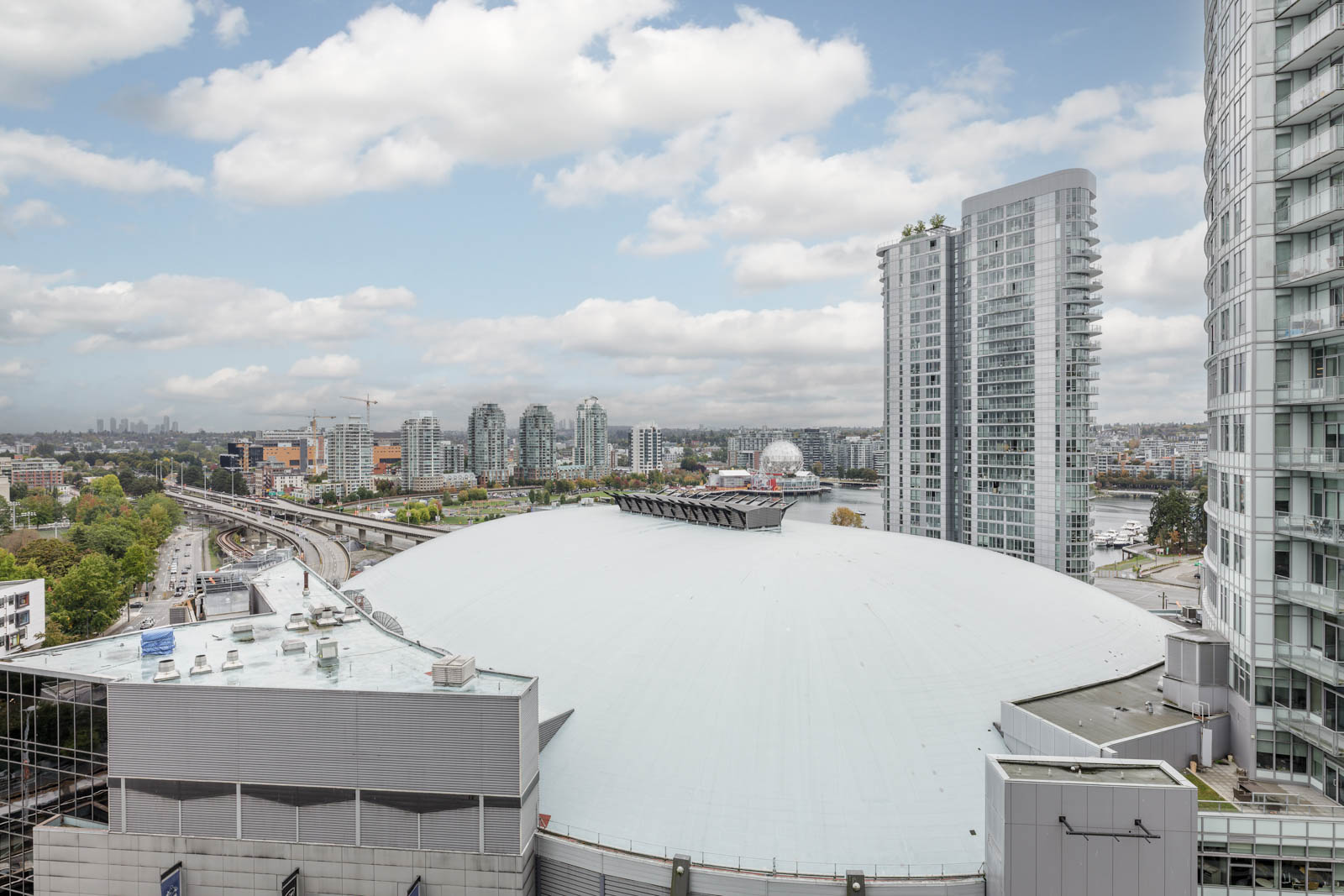 View of a large, white-domed building surrounded by modern high-rise apartments and cityscape under a partly cloudy sky.