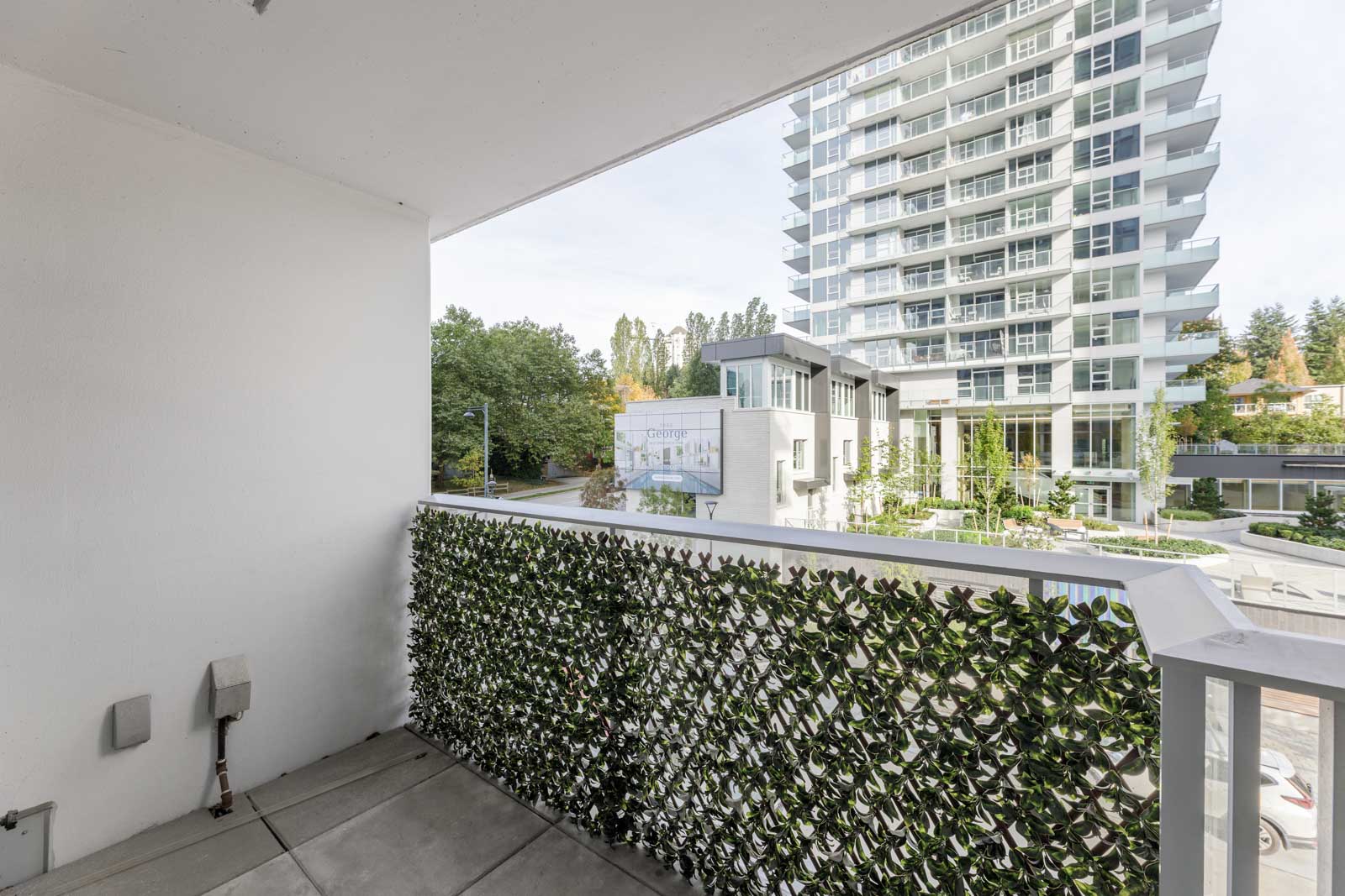 View from a balcony with a privacy screen, facing a modern high-rise apartment building and surrounding greenery.