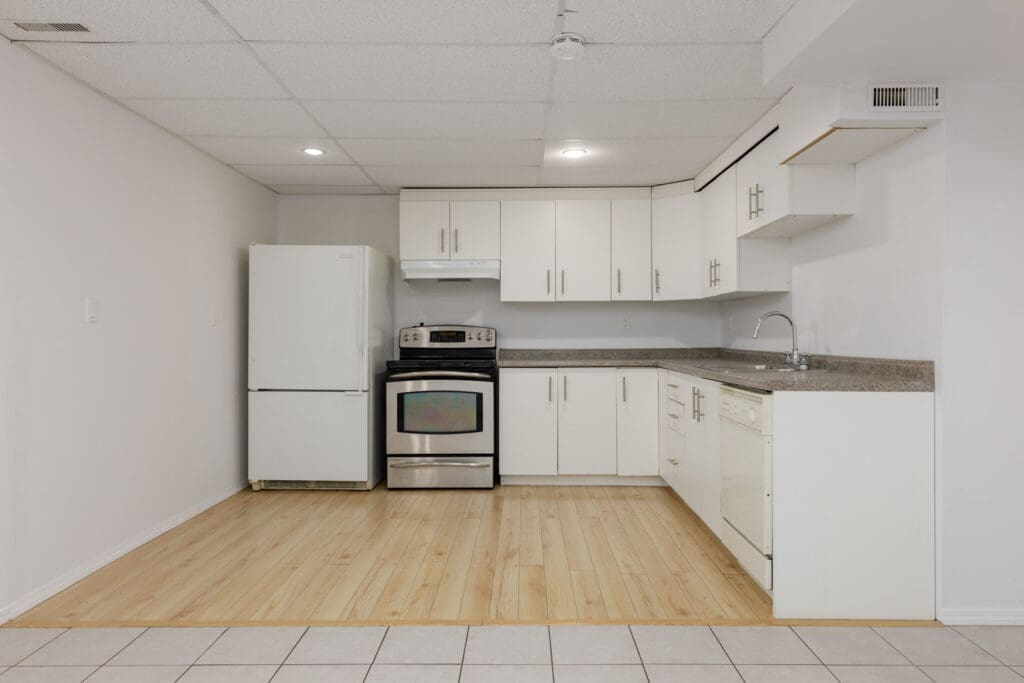Modern kitchen with white cabinets, stainless steel stove, white refrigerator, dishwasher, and a double sink. The floor transitions from tile to light wood.