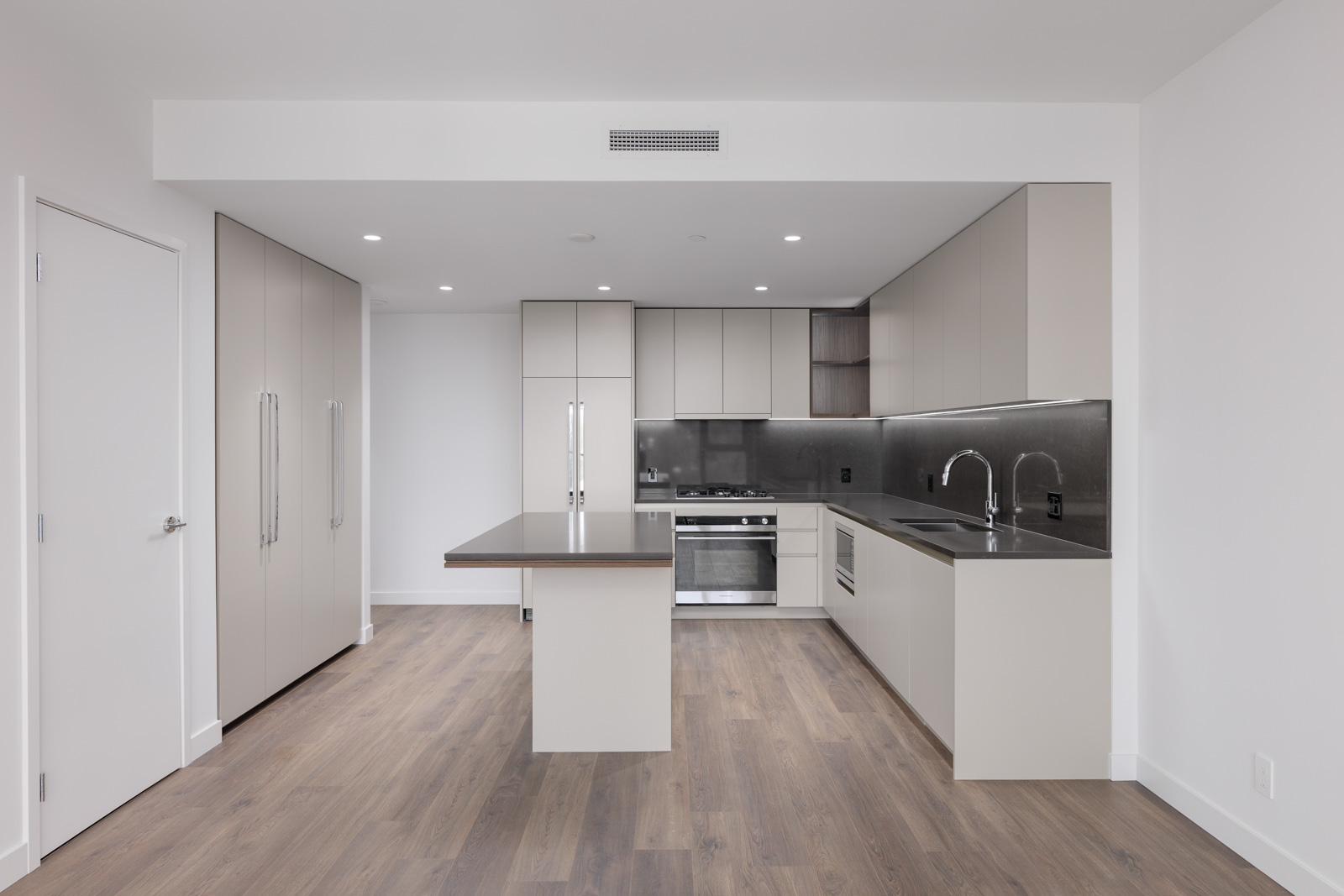 Modern kitchen with light cabinets, stainless steel appliances, an island with a built-in sink, and wood flooring in a minimalist, neutral-toned open space.